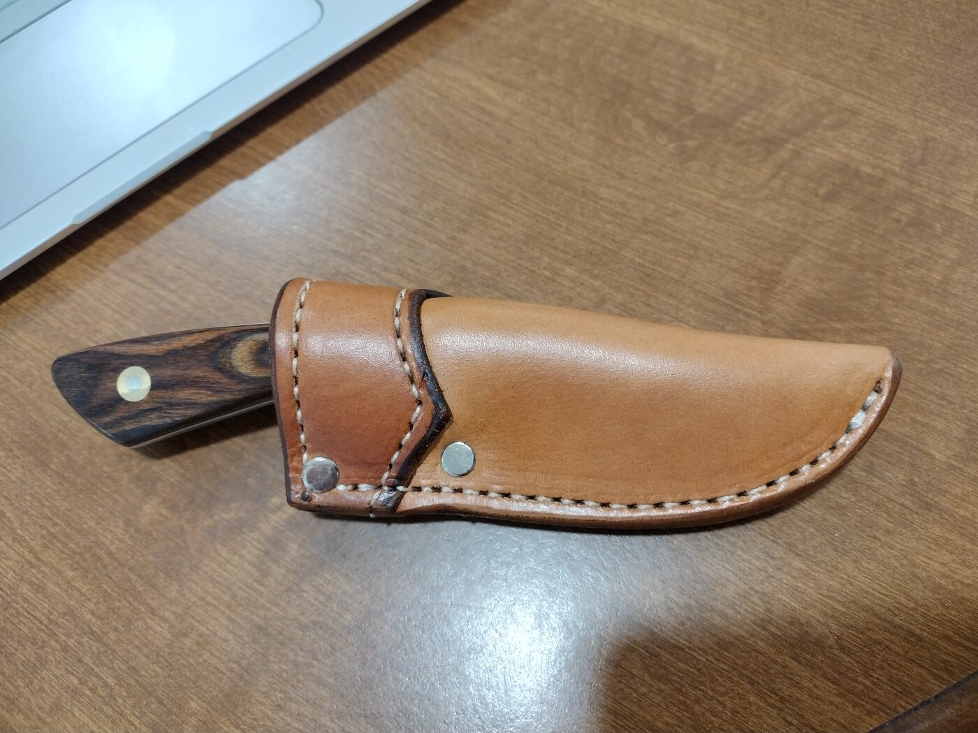 Basket-weave stamped scout carry sheath held in hand next to a knife with a bocote wood handle