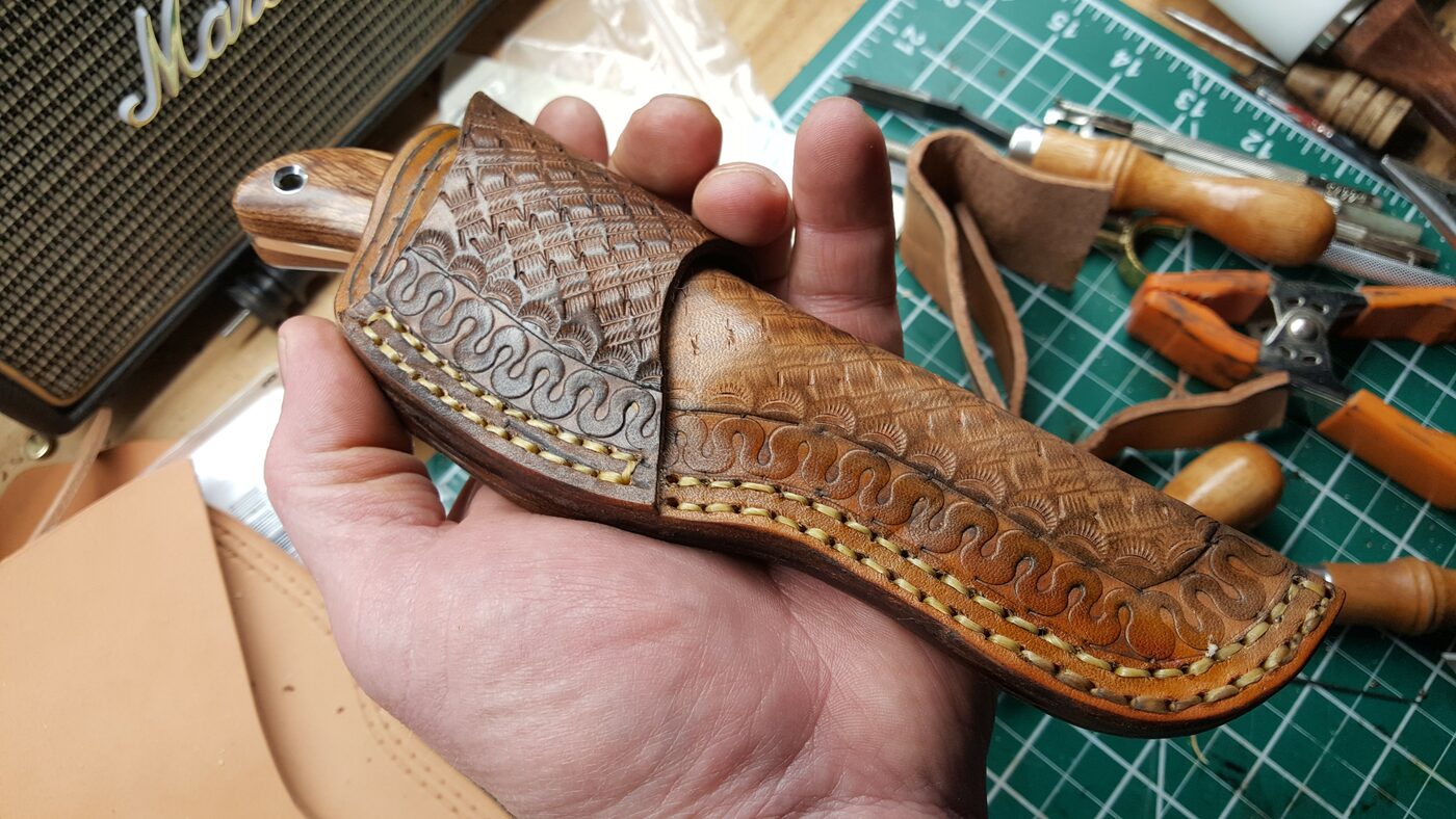 Scout carry sheath with visible hardware near the throat, next to a dark wood-handled knife